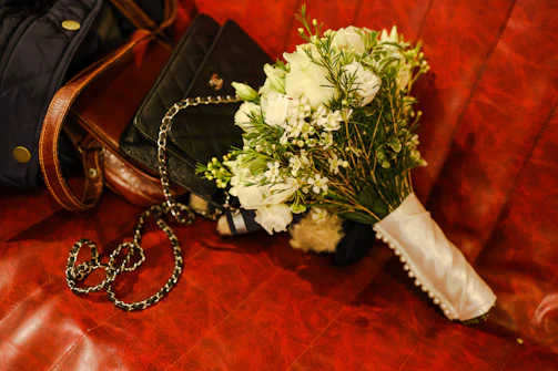 A glossy white clutch with intricate detailing placed beside a bouquet of fresh flowers.