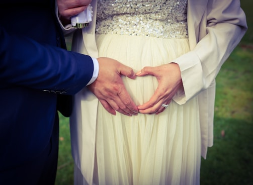 Two people are gently touching a pregnant belly. The hands are creating a heart shape over the belly, signifying love and expectation.