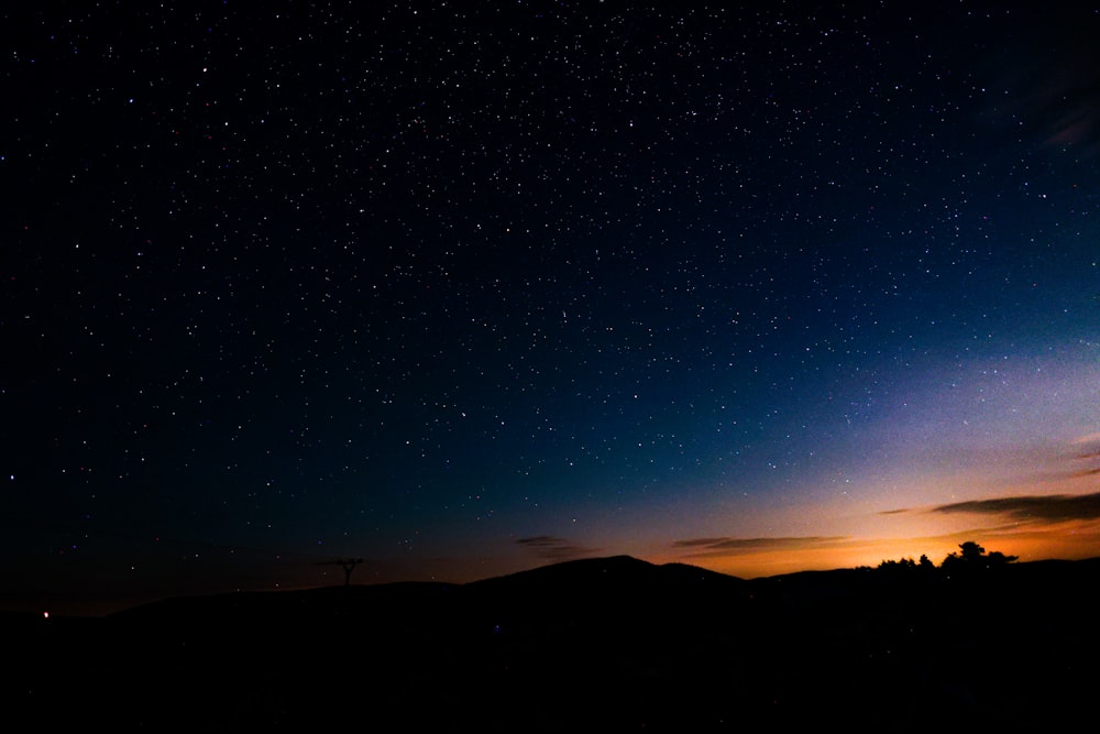 the night sky with stars above a hill