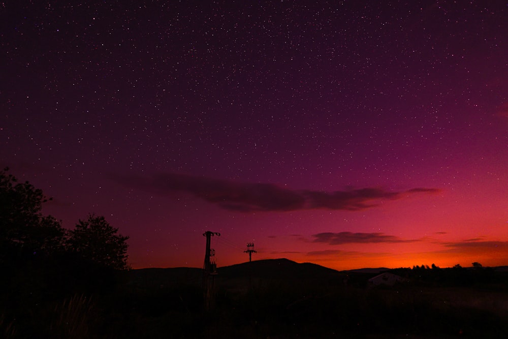 un cielo púrpura y rojo con estrellas sobre una colina