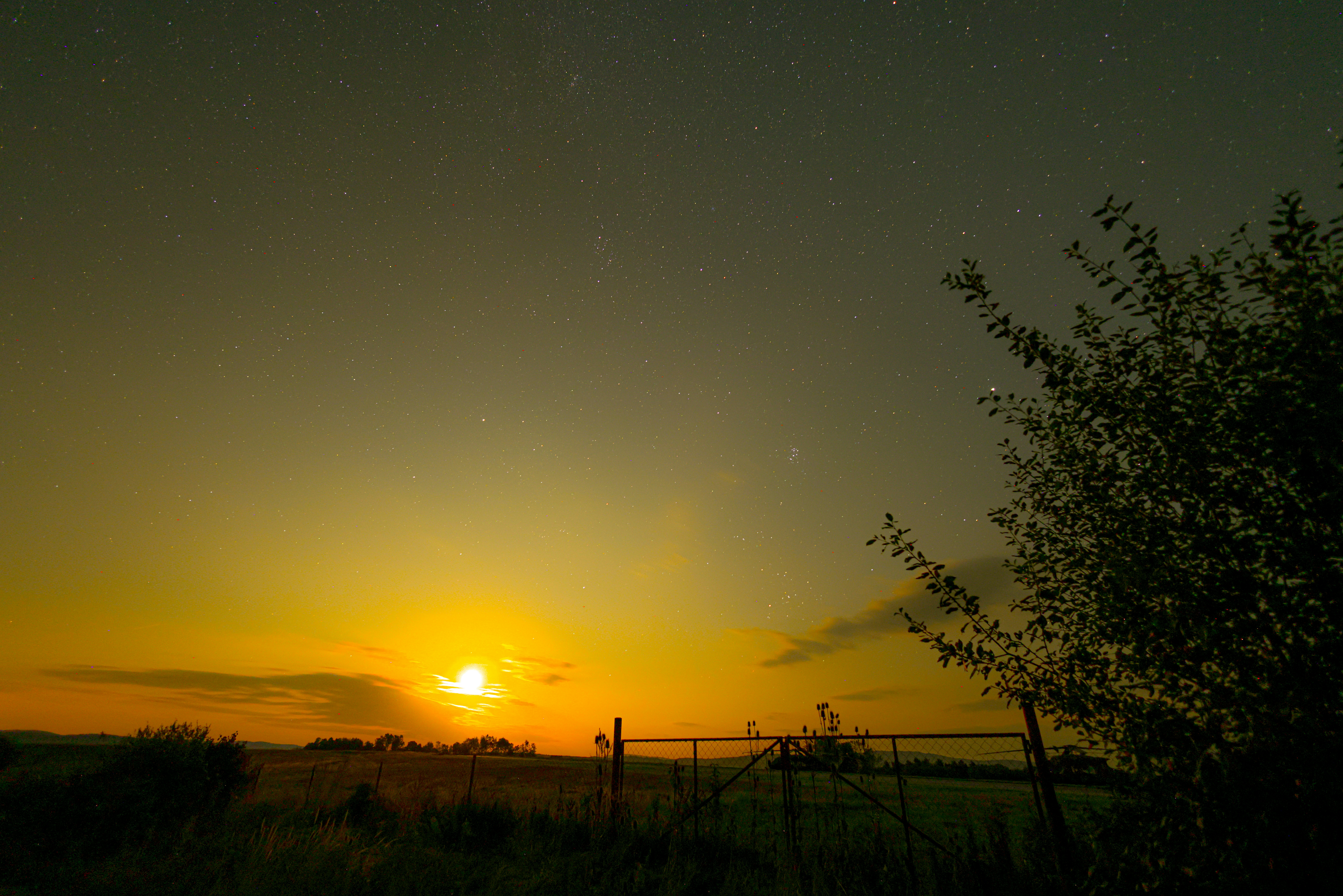 the sun is setting over a field with a fence