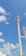 Two tall communication towers rise against a bright blue sky scattered with fluffy white clouds. The towers are equipped with multiple antennas and equipment, indicating their use for telecommunications. At the bottom left, part of a modern building and a streetlight are visible.