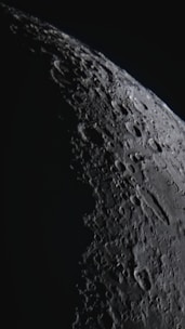 A close-up view of the moon's surface with detailed craters and rugged terrain, highlighted by contrasting light and shadow.