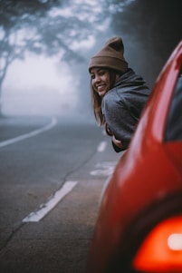 a woman leaning on a red car on a foggy day