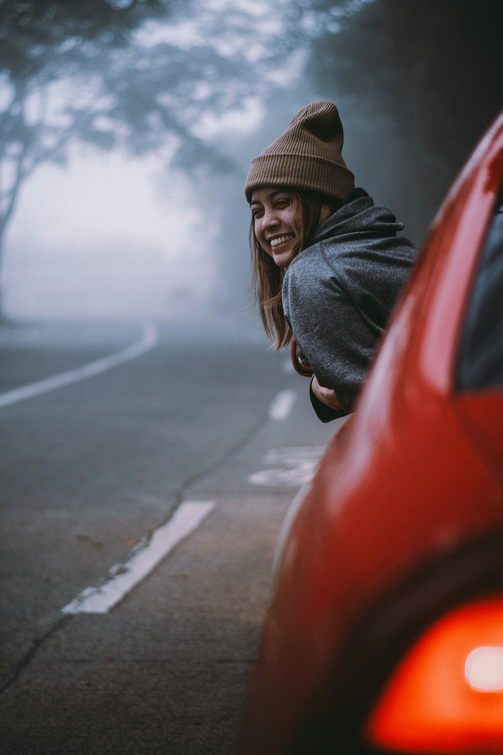 a woman leaning on a red car on a foggy day