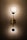 An elegant wall light fixture with a modern design is mounted on a patterned wallpaper. The lamp consists of two circular lights connected by a vertical rod, casting a warm glow that highlights the intricate texture of the background.