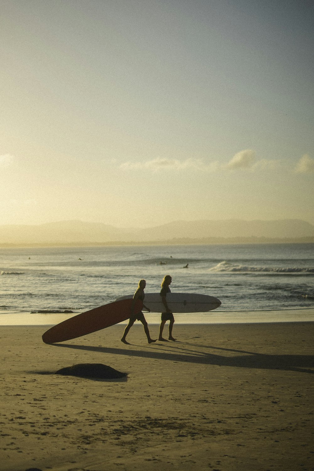 two people walking on a beach with a surfboard