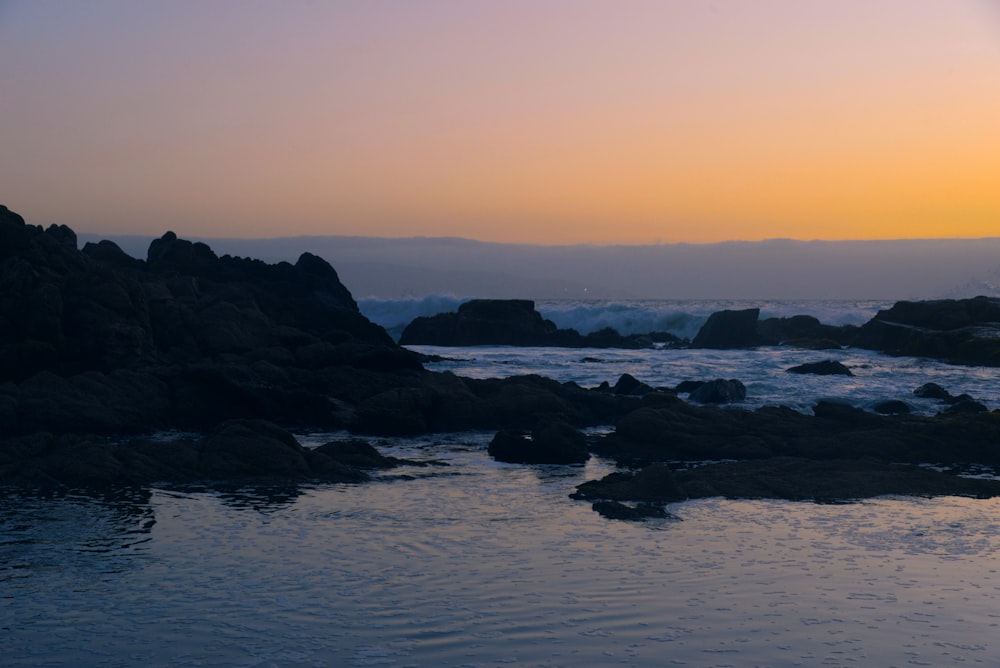 a body of water surrounded by rocks at sunset