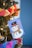 A decorated Christmas tree with a handmade snowman card hanging on it. The snowman is wearing a black hat and a colorful scarf. Surrounding the card are various colored paper chains and festive lights, creating a cheerful holiday atmosphere.