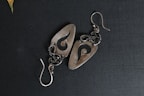 Pair of handcrafted earrings with intricate patterns displayed on a rustic background