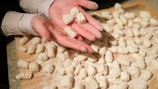 Close-up of hands skillfully rolling fresh pasta dough on a wooden board.