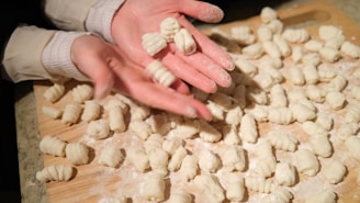 Close-up of hands rolling fresh pasta dough on a wooden board dusted with flour.