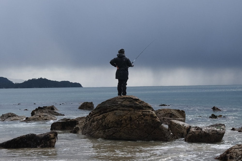 a man standing on top of a rock next to the ocean