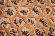Intricate floral patterns in terracotta are set into a beige cement background, forming a geometric lattice. Each section features unique, detailed natural motifs such as flowers and leaves, showcasing artistic craftsmanship.