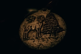 A carved ornament featuring a deer and a pine tree against a dark background, highlighting intricate details and textures in the natural design.