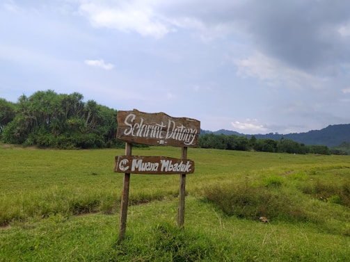 A welcoming farm entrance with a rustic wooden sign saying 'One Acre Farm, LLC' surrounded by green fields and a clear sky.