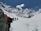 A group of hikers is trekking through a snowy mountainous landscape under a clear blue sky. The snow-covered mountains loom majestically in the background, while the hikers wear colorful gear and carry backpacks. The scene suggests a challenging and adventurous journey through pristine, untouched nature.