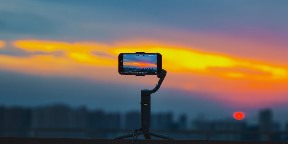a cell phone sitting on a tripod with a sunset in the background