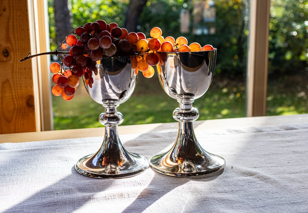 two silver goblets filled with grapes on a table