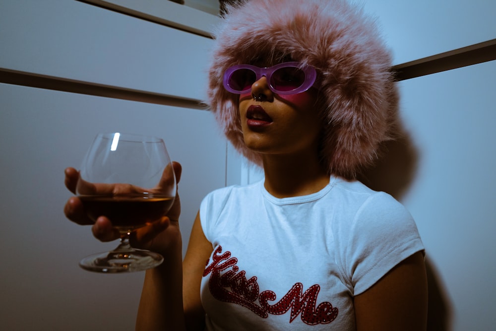 a woman wearing a fur hat and glasses holding a wine glass