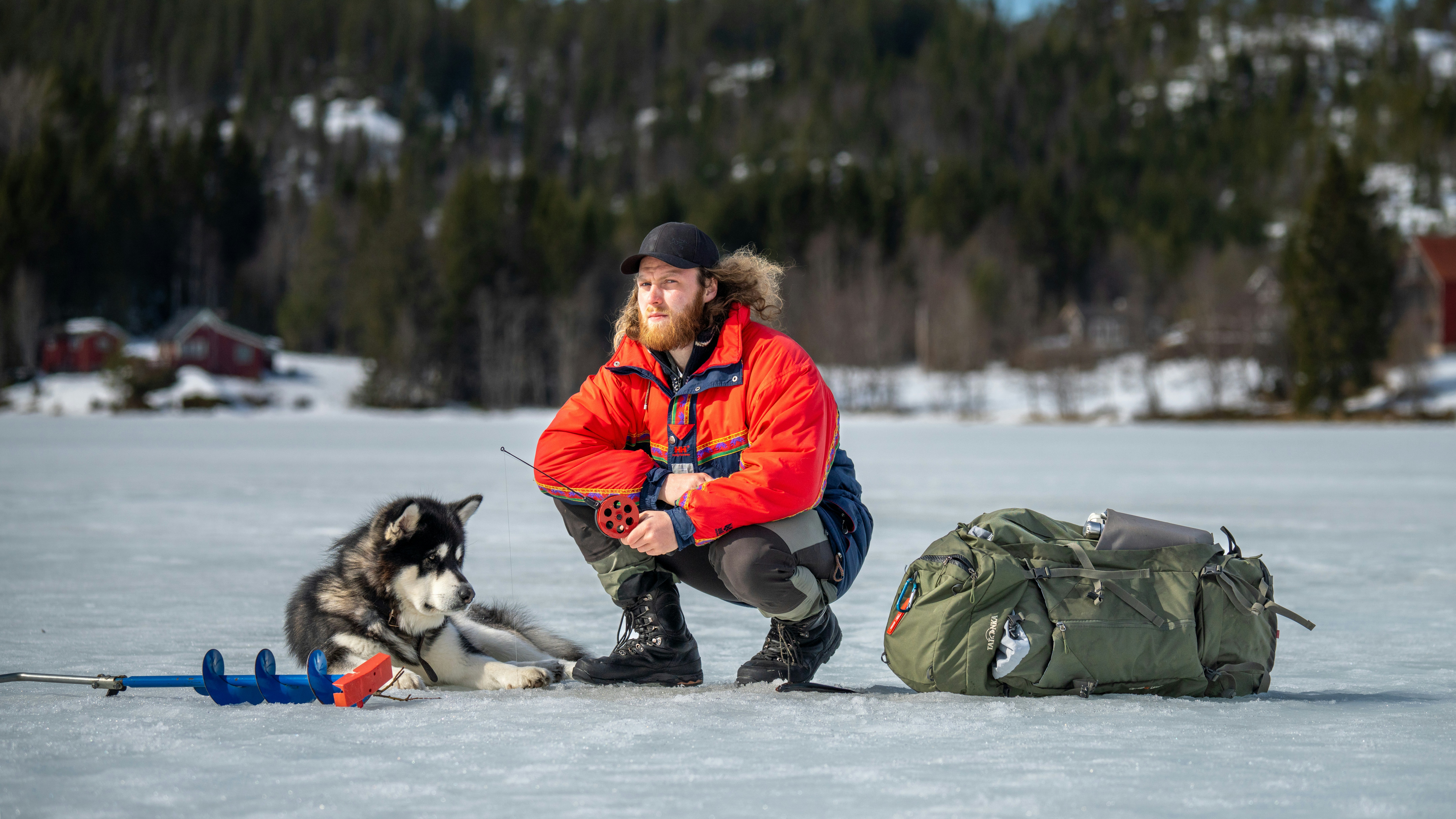 a man kneeling down next to a dog on a snow covered field