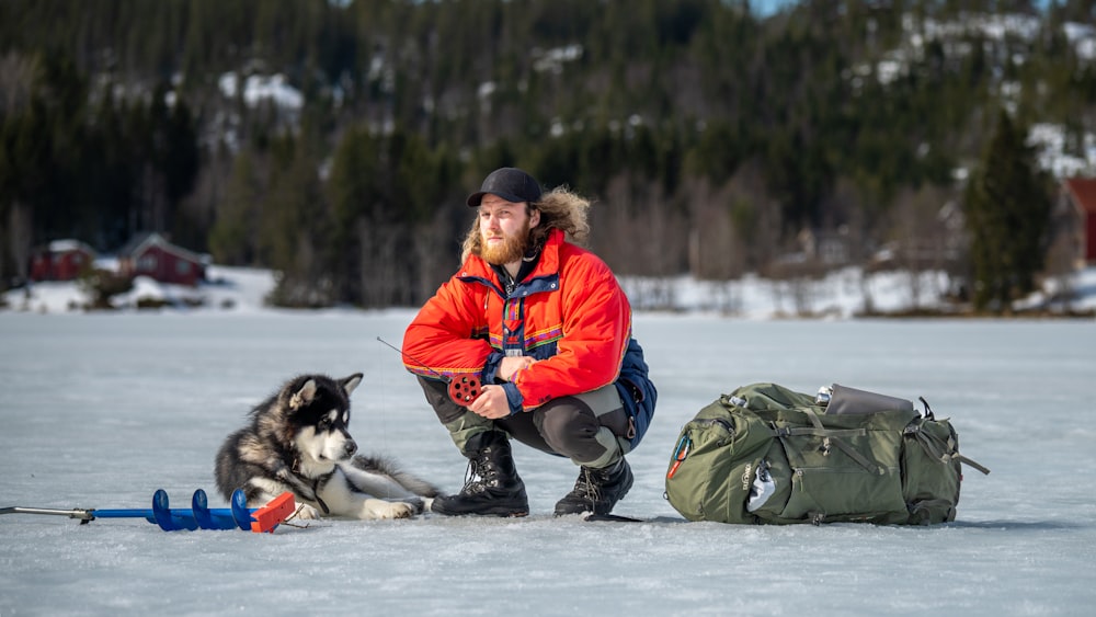 a man kneeling down next to a dog on a snow covered field