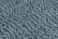 A close-up view of a textured surface featuring numerous smooth, oval stones embedded in concrete. The stones are dark grey and arranged in a pattern that creates a sense of movement and rhythm across the surface.