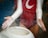 A person clad in a red leotard with white sleeves applies chalk to their hands above a white chalk bowl. Chalk particles are visibly dispersing into the air, demonstrating preparation and focus.