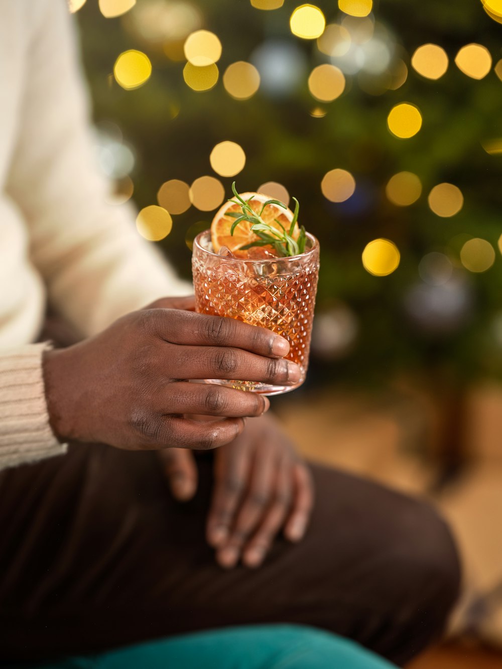 a person holding a drink in front of a christmas tree