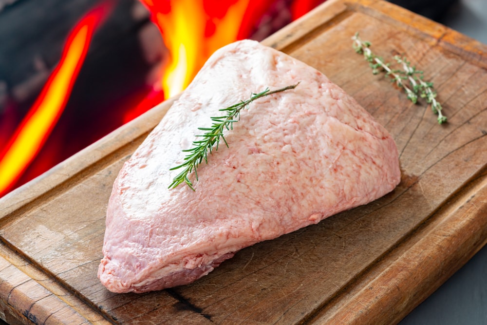 a piece of meat on a cutting board with a sprig of rosemary