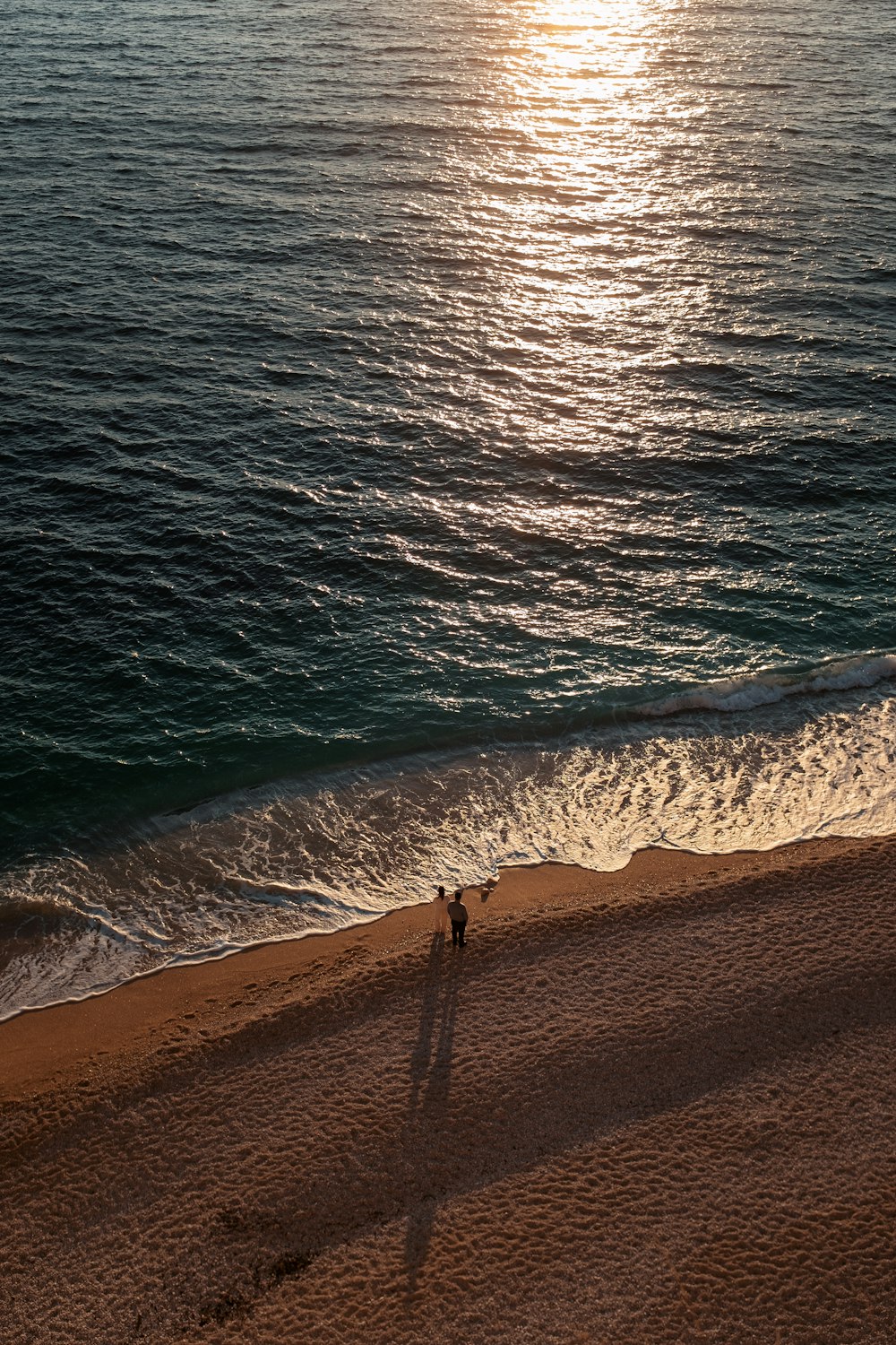 a couple of people standing on top of a sandy beach