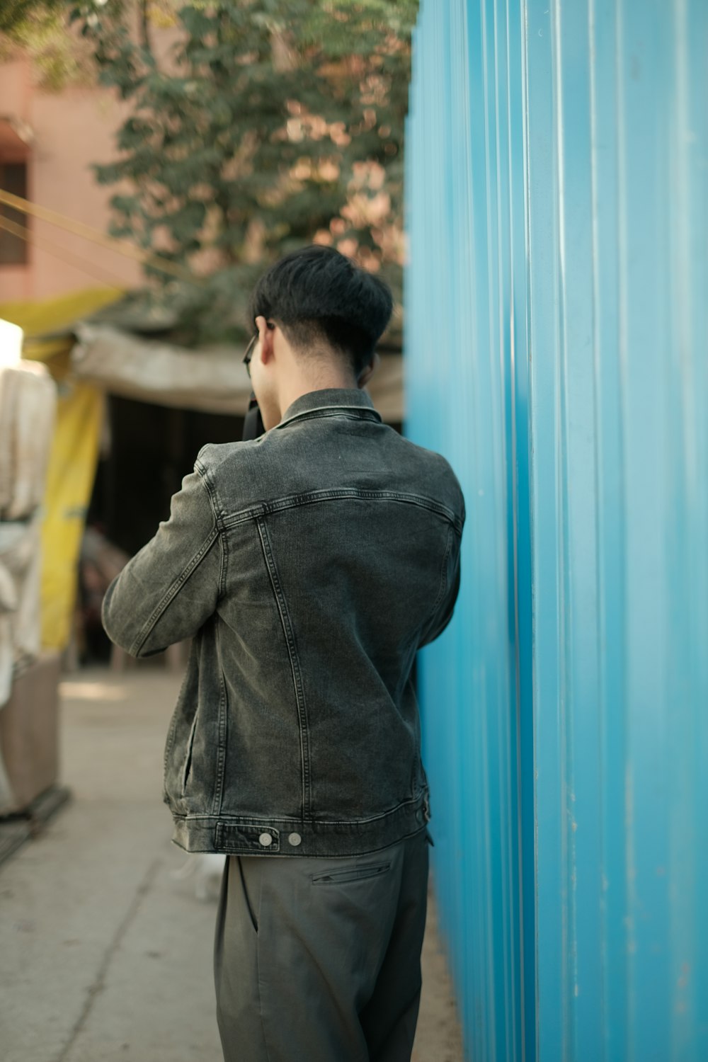 a man leaning against a blue wall talking on a cell phone