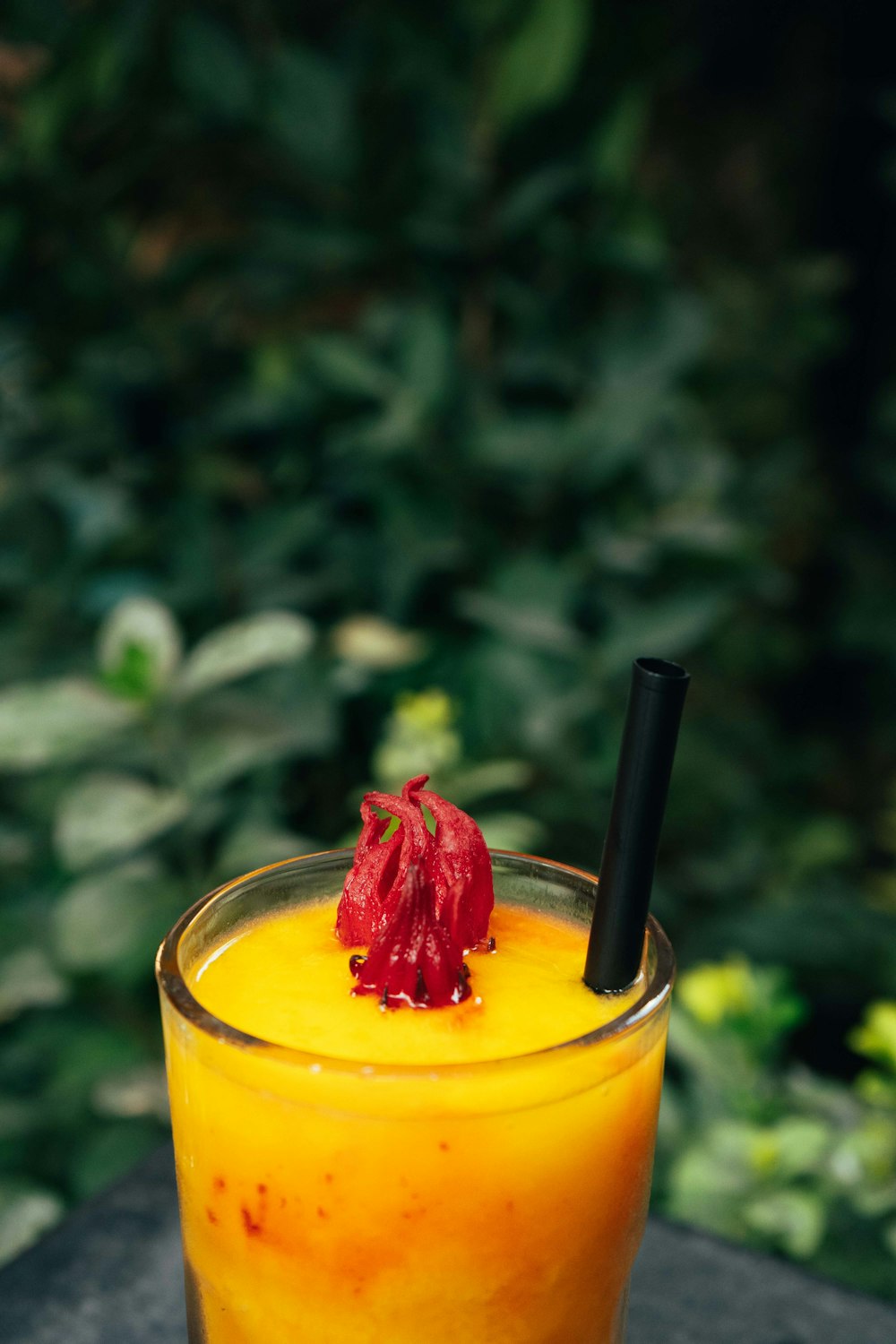 a glass of orange juice with a red flower on top