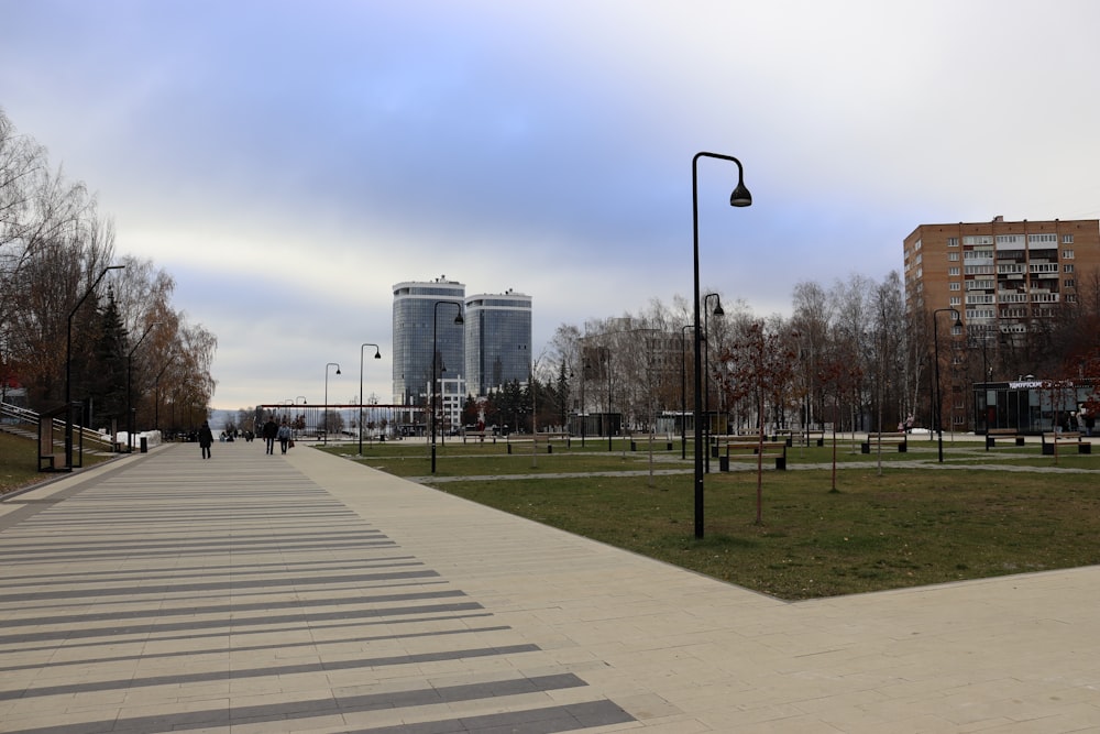 a walkway in the middle of a park with tall buildings in the background