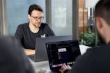 Man with glasses working on a laptop in a bright coworking space.