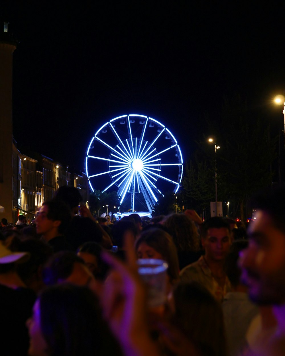 a crowd of people standing around a ferris wheel at night