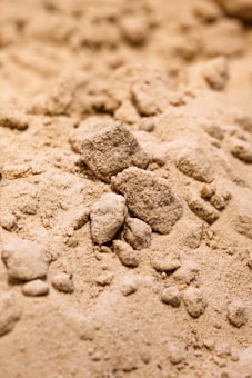 A close-up view of a pile of fine, powdery sand with several small, irregularly shaped clumps and grains visible. The texture appears soft and granular.