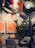 A cozy indoor setting featuring modern decor with two abstract orange paintings on the wall. A small round table is surrounded by stylish chairs, with a potted plant adding greenery to the space. The ceiling is adorned with spherical lights and festive garlands accented by bright red ribbons.