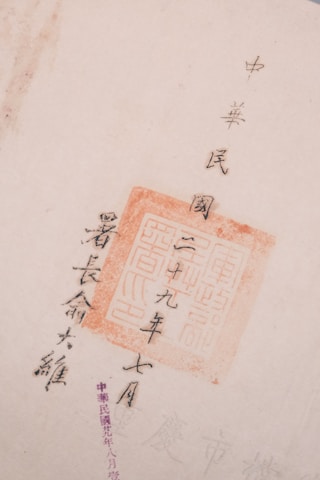 The image features Chinese calligraphy with a red stamp seal, showcasing traditional characters on a light-colored paper. The text is arranged vertically and accentuated by the vivid red of the stamp.