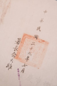 The image features Chinese calligraphy with a red stamp seal, showcasing traditional characters on a light-colored paper. The text is arranged vertically and accentuated by the vivid red of the stamp.