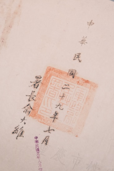 The image features Chinese calligraphy with a red stamp seal, showcasing traditional characters on a light-colored paper. The text is arranged vertically and accentuated by the vivid red of the stamp.