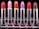 A row of six lipsticks in varying shades displayed against a black background. The lipsticks are housed in metallic silver tubes, with colors including red, pink, orange, and brown. Each lipstick has a distinct color, creating a gradient effect.