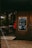A charming outdoor cafe setting with wooden walls and decor. It features a chalkboard menu with festive illustrations and the text written in Russian. The entrance has wicker chairs and tables, creating a cozy and inviting atmosphere.