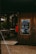 A charming outdoor cafe setting with wooden walls and decor. It features a chalkboard menu with festive illustrations and the text written in Russian. The entrance has wicker chairs and tables, creating a cozy and inviting atmosphere.