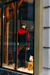 A storefront display features a mannequin dressed in a red and black ski outfit, complete with goggles and holding a snowboard. The scene is set against a snowy background with decorative logs and artificial snow, creating a winter sports theme.