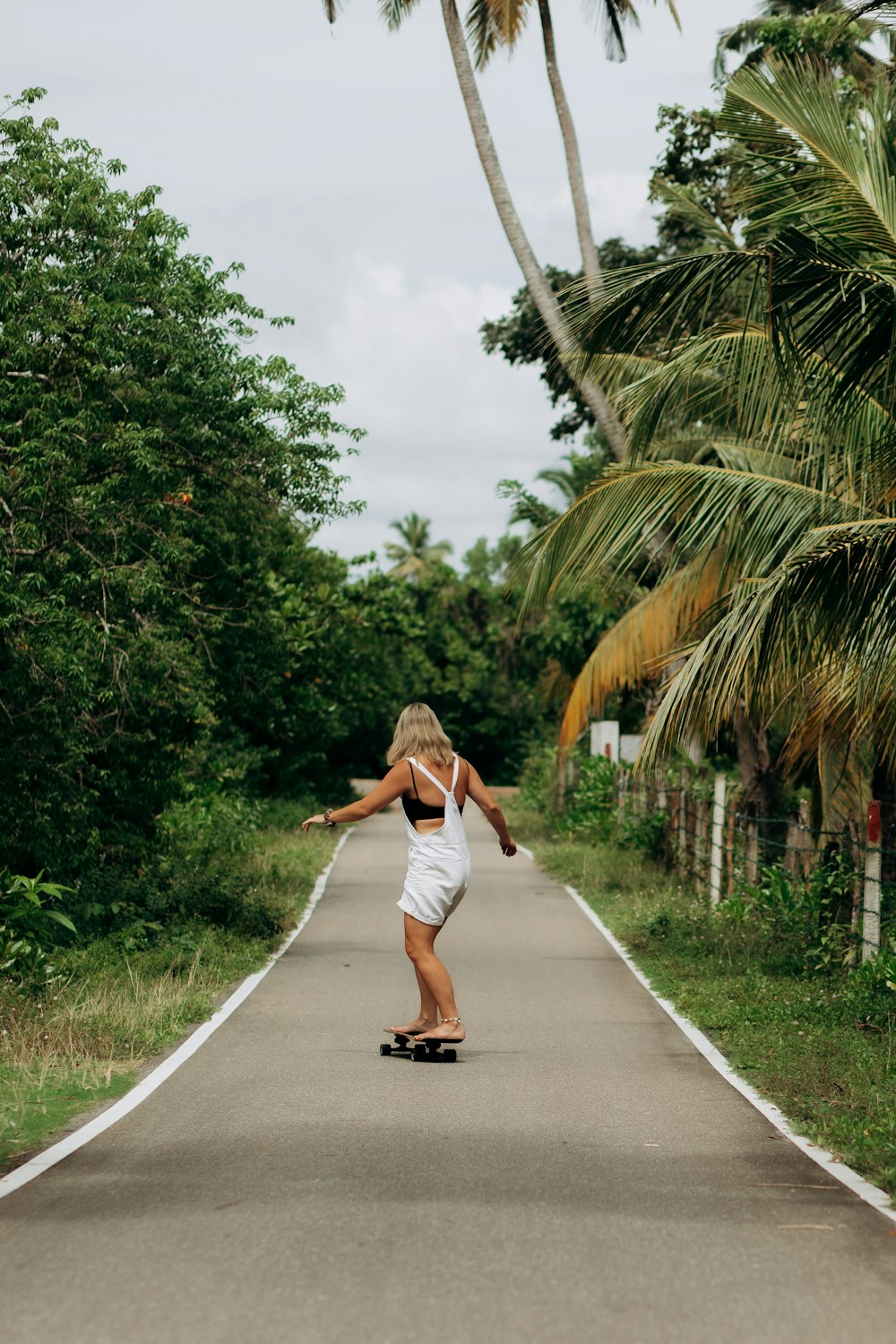 a woman riding a skateboard down a road next to palm trees