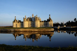 Elegant white walls and ornate windows of Hluboká Castle reflecting in a calm pond.