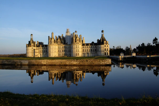 Elegant white walls and ornate windows of Hluboká Castle reflecting in a calm pond.
