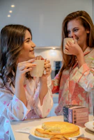 A cheerful caregiver and client sharing a laugh over a cup of tea at a kitchen table.