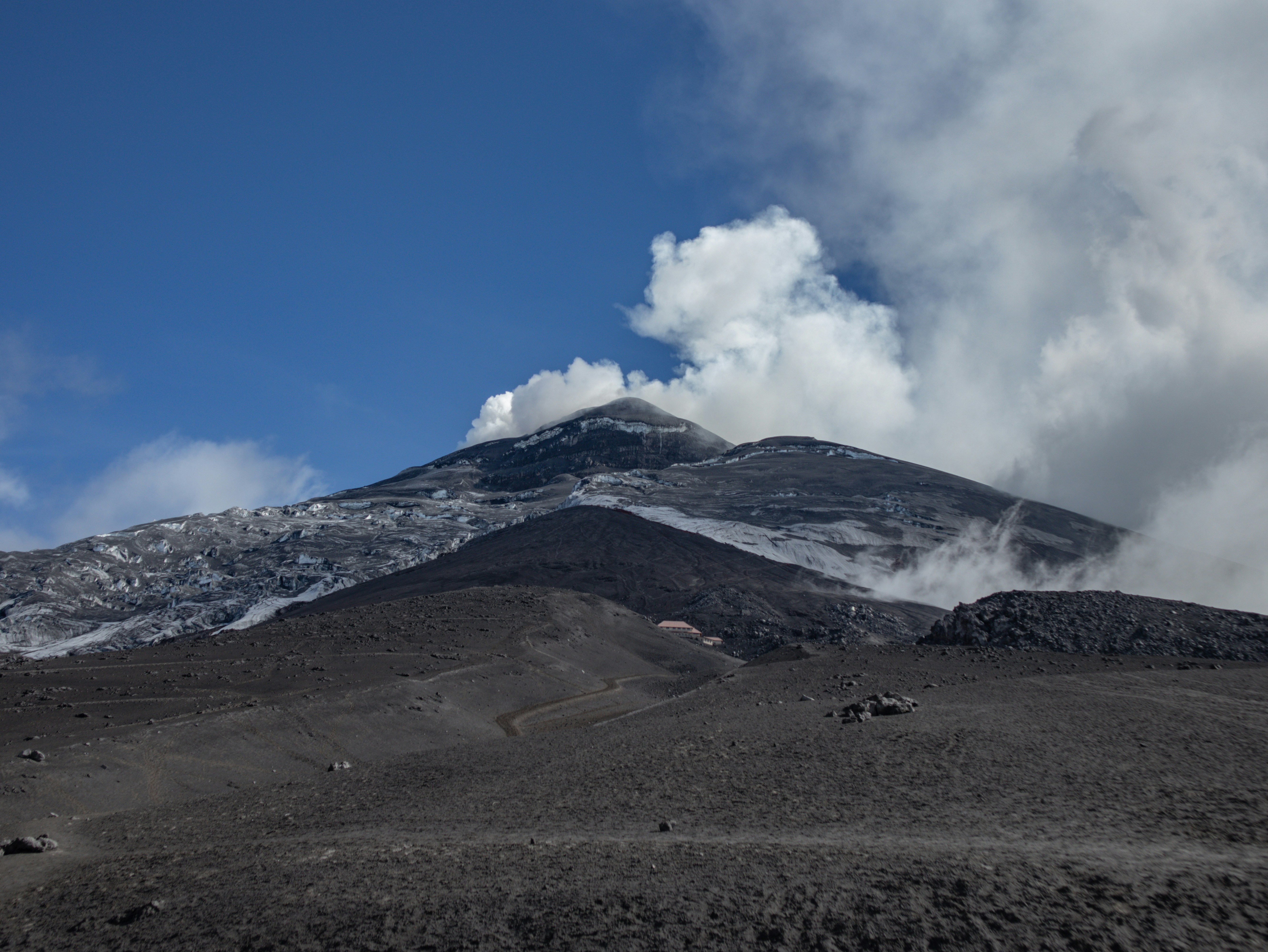 a mountain covered in snow and clouds under a blue sky